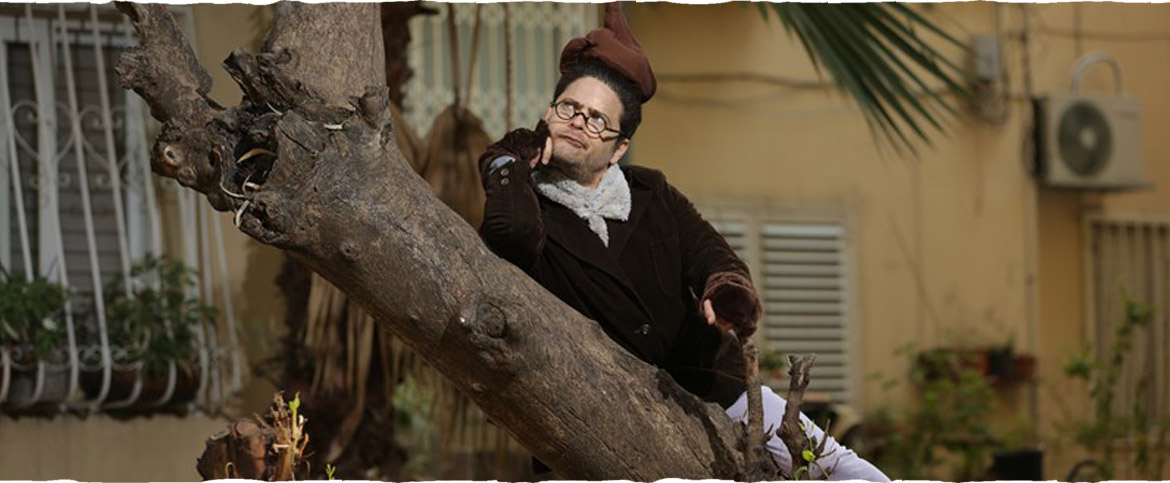 צילום מתוך ההצגה "החולד הקטן" - הדמות הראשית נשענת על גזע עץ ומהרהרת מי עשה לו על הראש.
